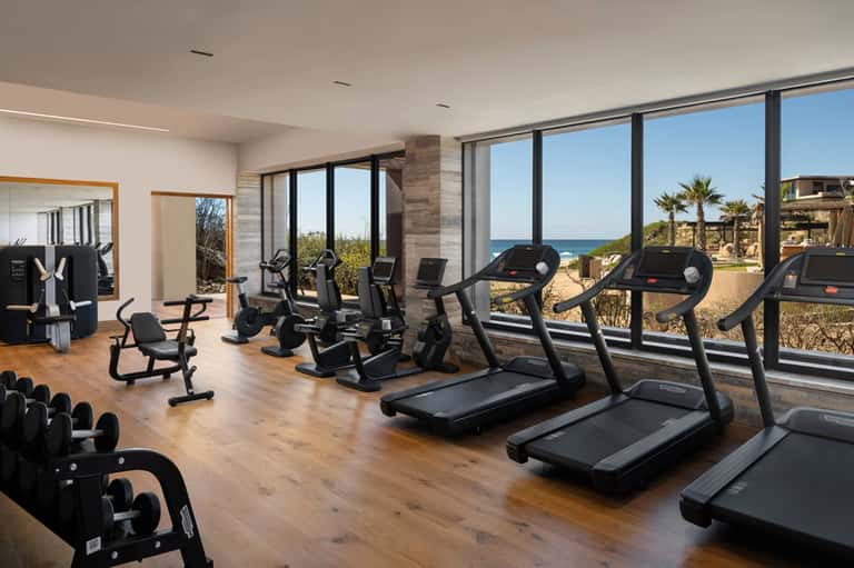 Beachfront fitness center with treadmills, exercise bikes, and expansive ocean views through windows