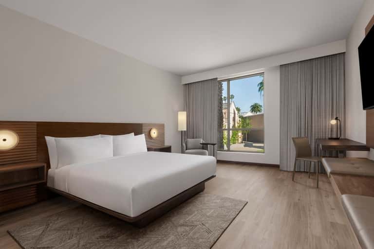 Modern hotel bedroom with king bed, balcony, contemporary furnishings, and warm lighting