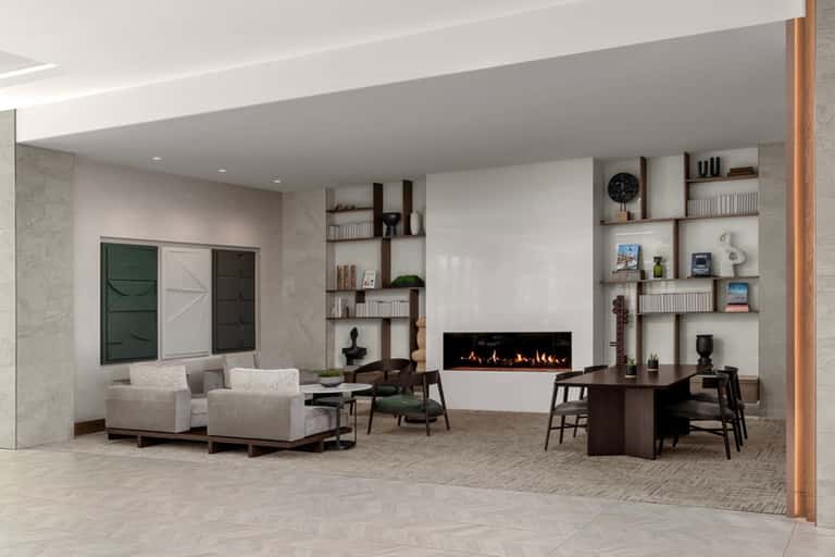 Contemporary hotel lobby with fireplace, floating shelves, cream armchairs, and modern furnishings