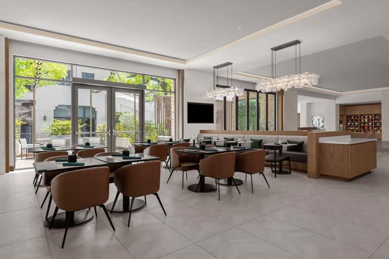Contemporary hotel lobby with dining area, earth-tone seating, crystal chandeliers, and large windows