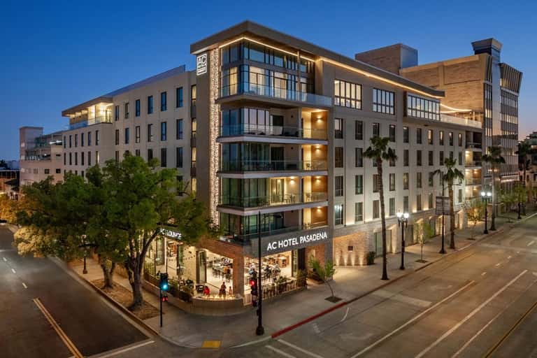 Modern AC Hotel Pasadena building at dusk with illuminated windows, glass balconies, and street level retail
