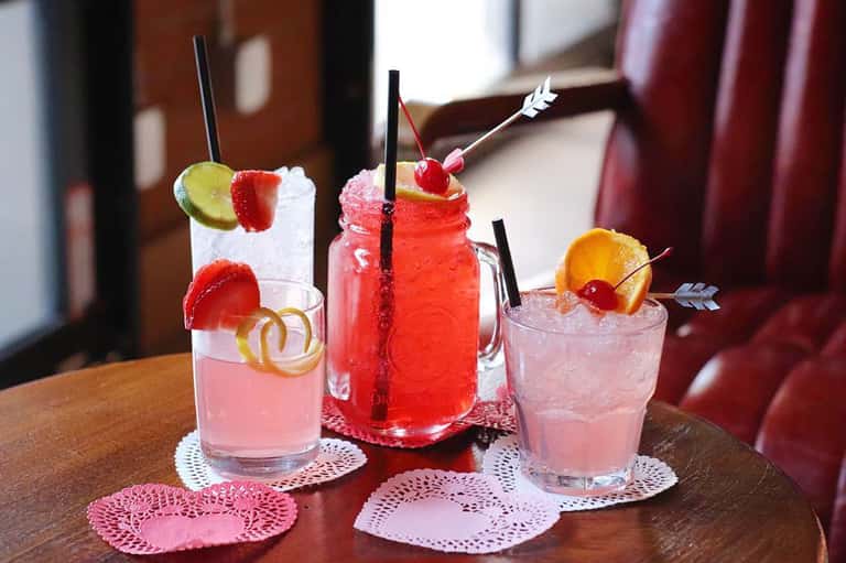 Three colorful tropical cocktails with fruit garnishes on pink doilies at resort bar