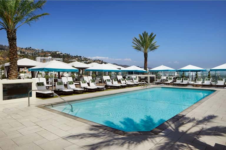 Resort rooftop pool with blue water, turquoise umbrellas, white loungers, and mountain views