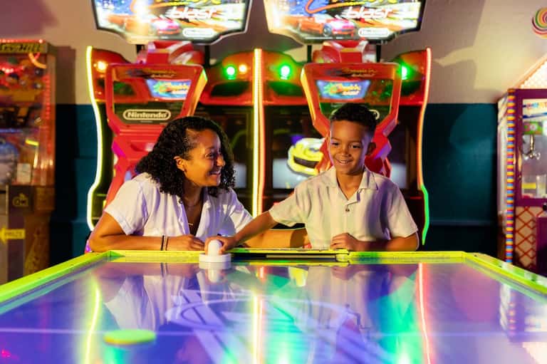 Children playing arcade games and air hockey in brightly lit game room with neon lighting