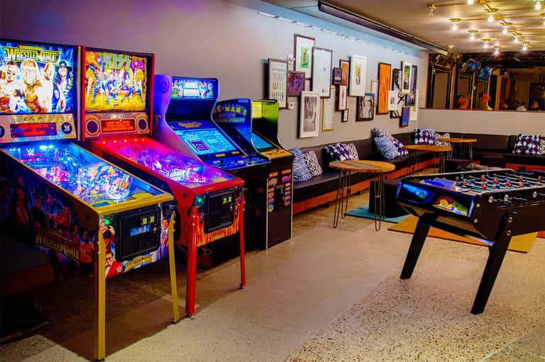 Game room with vintage arcade machines, pinball tables, foosball, and colorful neon lighting