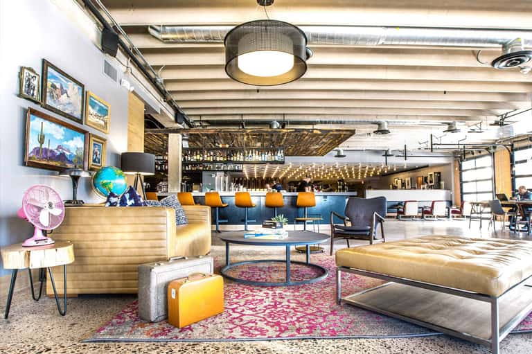 Contemporary hotel lobby with colorful furnishings, bar area, and eclectic artwork on white walls