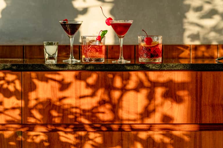 Craft cocktails displayed on wooden bar counter with cherry garnishes and tropical drinks