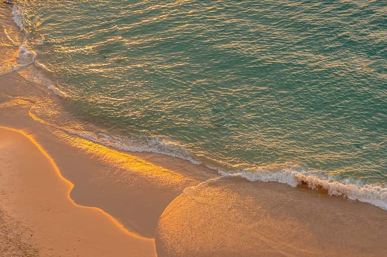 Golden hour beach scene with gentle waves, turquoise water, and pristine sandy shoreline