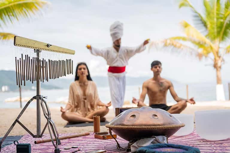 Beach wellness retreat with yoga instructor and participants, meditation gong, ocean backdrop