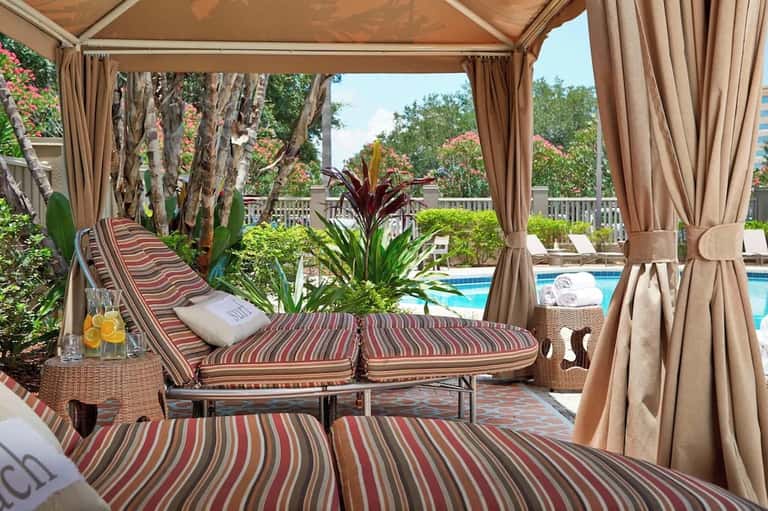 Luxurious poolside cabana with striped loungers, sheer curtains, tropical plants, and pool view
