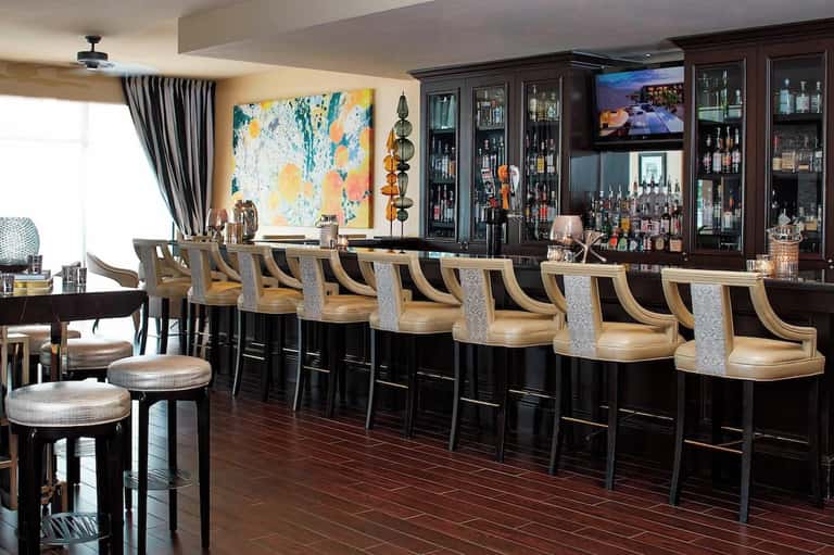 Upscale hotel bar with dark cabinetry, wooden countertop, and extensive liquor collection