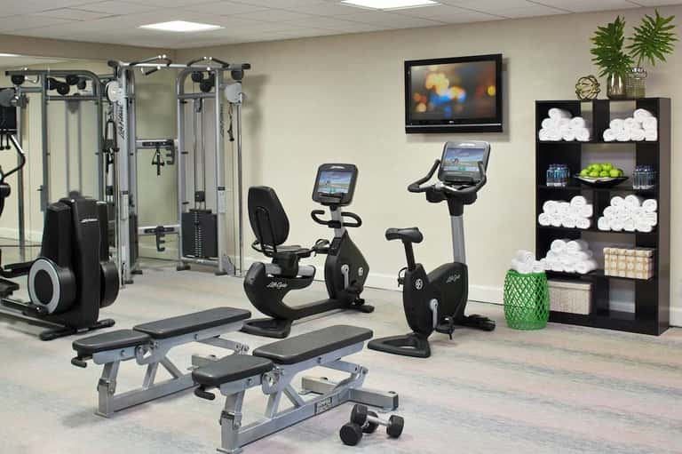 Compact fitness room with exercise machines, stationary bikes, weight benches, and towel storage shelving