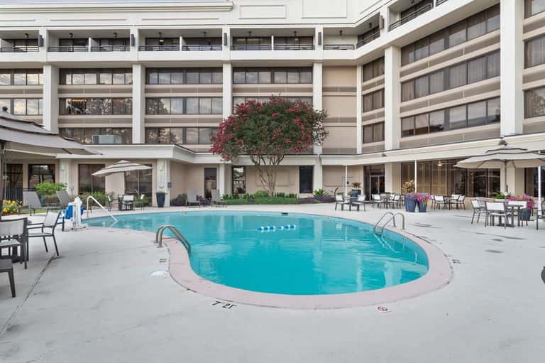 Resort courtyard with curved swimming pool, lounge chairs, flowering tree, and multi-story building