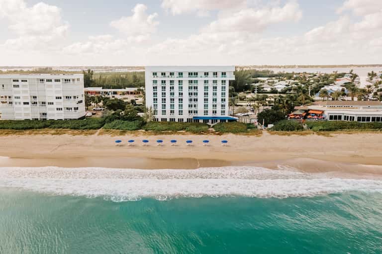 Beachfront resort building with white facade and blue umbrellas on sandy beach with ocean waves