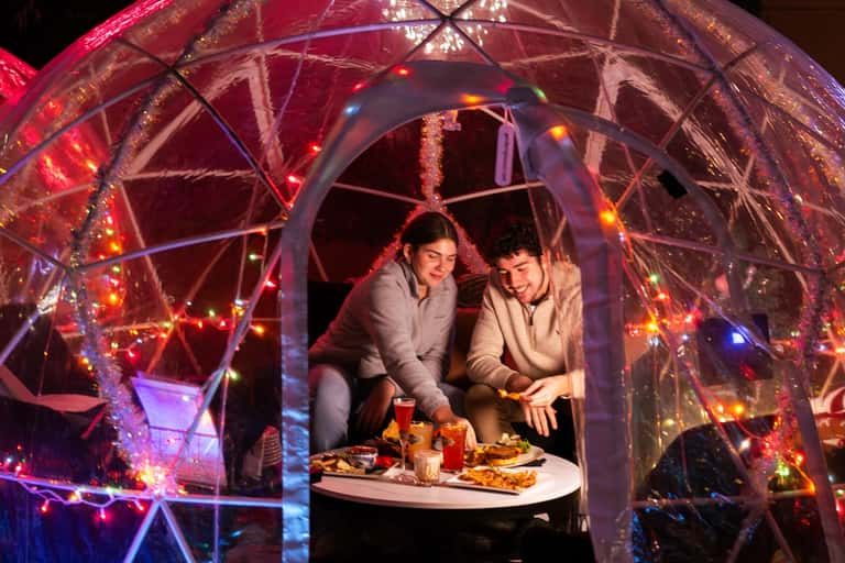 Illuminated outdoor dining pod with colorful lights and couple inside