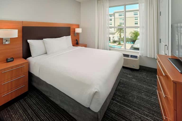 Hotel bedroom with orange headboard, white bedding, pool view, and modern furnishings
