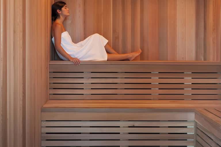 Woman in white towel relaxing in wooden sauna with vertical wood paneling