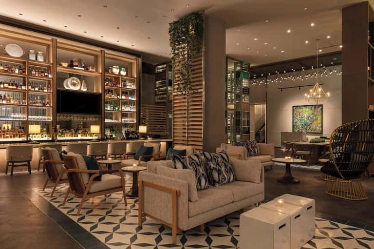 Sophisticated lounge with bar shelving, neutral furniture, patterned rug, and warm lighting