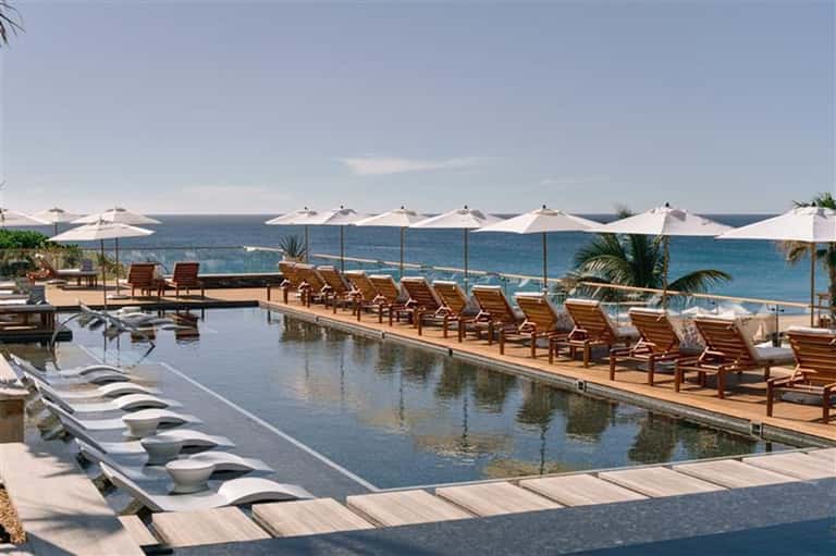 Beachfront infinity pool with ocean views, lounge chairs, and white umbrellas