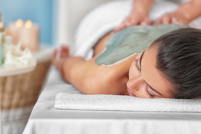 Spa massage therapist applying facial treatment to relaxed client in treatment room