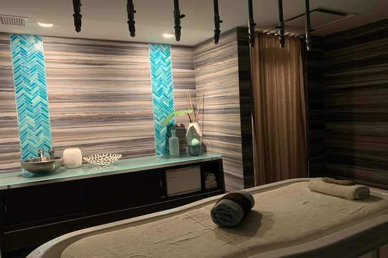 Modern spa massage room with turquoise tile accents, treatment bed, and mood lighting