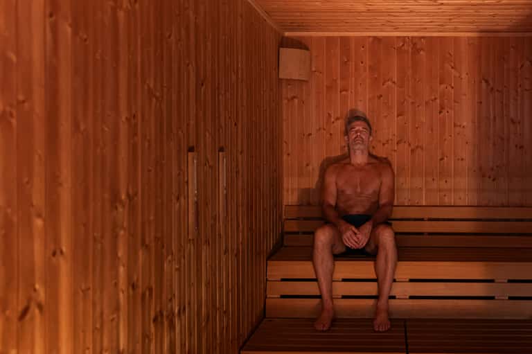 Man relaxing in wooden sauna with traditional heated wooden interior and benches