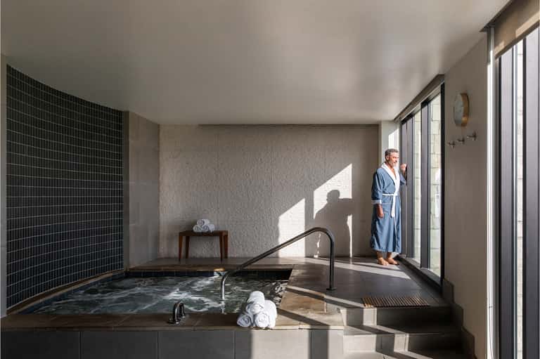 Spa area with sunken soaking tub, black tile wall, glass doors opening to patio, and natural light
