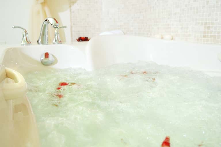 Luxurious bathtub filled with bubbles and rose petals with chrome faucet and tile walls