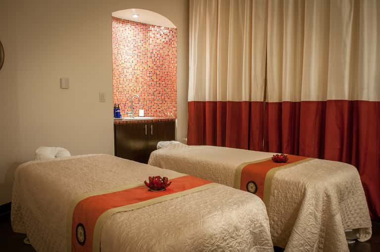 Spa treatment room with two massage beds, mosaic tile feature wall, and elegant curtain partitions