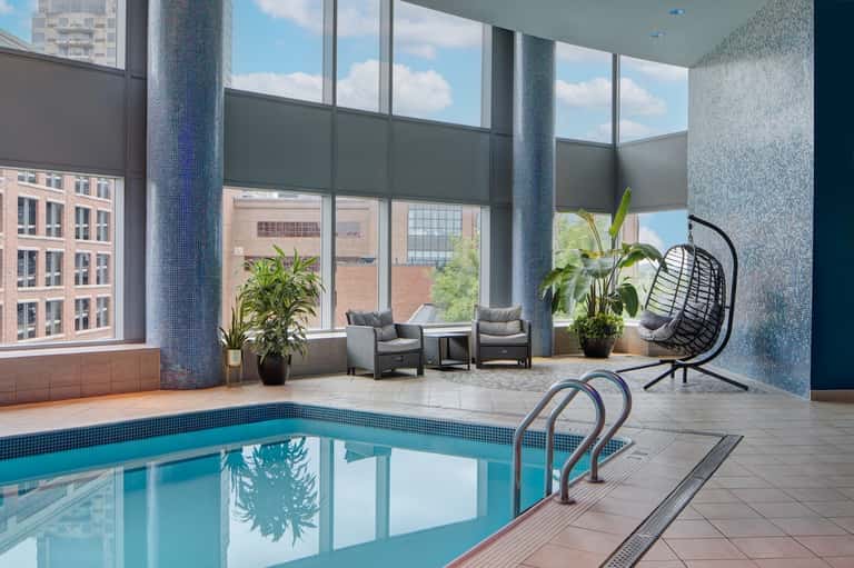 Indoor pool with large windows, city views, lounge chairs, and contemporary furnishings