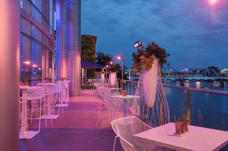 Waterfront bar and lounge with pink lighting, modern seating, and river bridge views