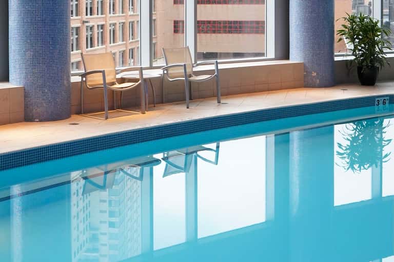 Indoor pool with blue water, large windows overlooking city, modern deck seating area