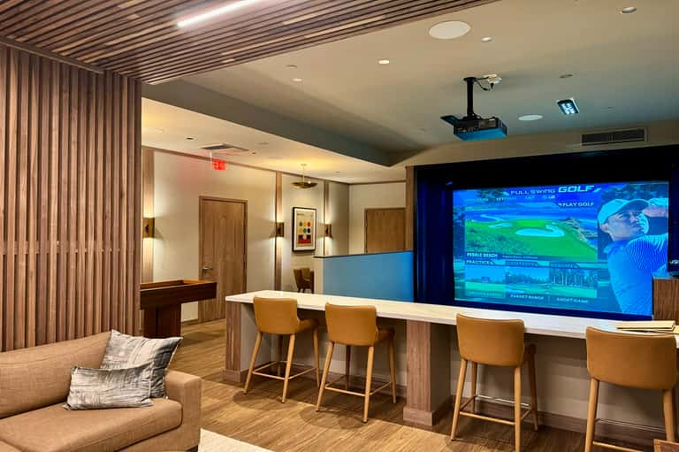 Game room with golf simulator screen, bar seating, and wood paneling