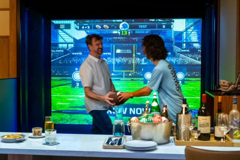 Hotel room entertainment area with two people watching interactive sports game on large screen