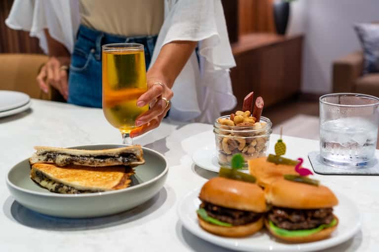 Guest holding iced beverage at resort dining table with appetizers and sandwiches
