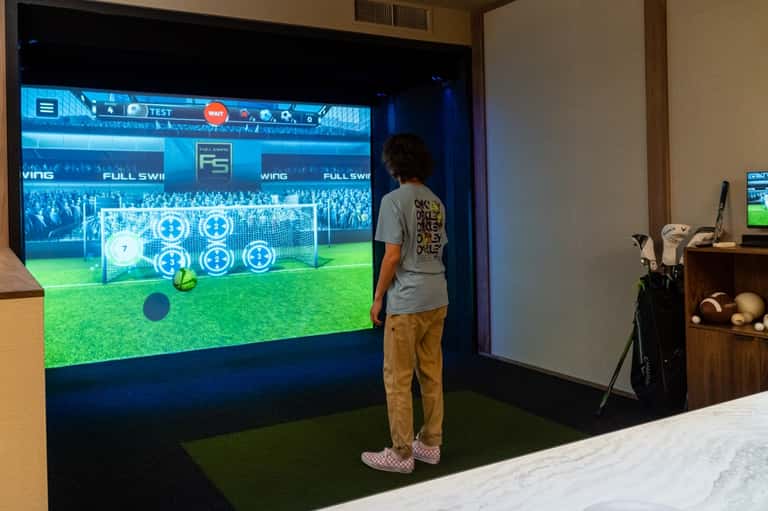 Man using interactive golf simulator screen with virtual course display and golf equipment nearby