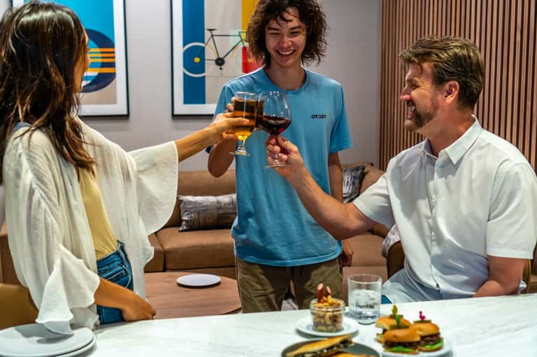 Three guests toasting with drinks in modern hotel room with casual furnishings and colorful artwork
