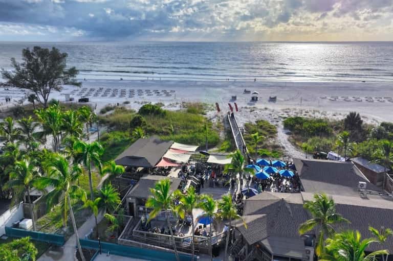 Beachfront resort with umbrellas on sand, palm trees, and ocean boardwalk