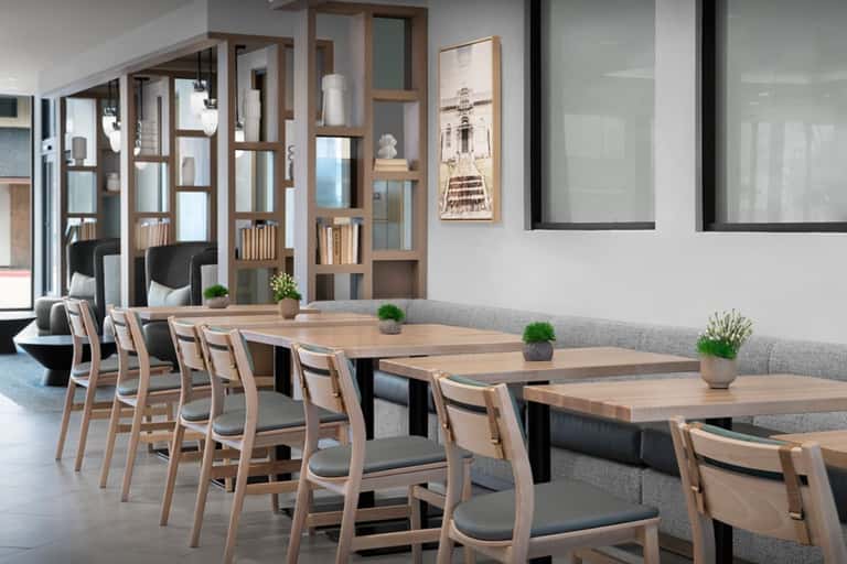 Modern meeting room with long wooden tables, light wood chairs, and glass partitions