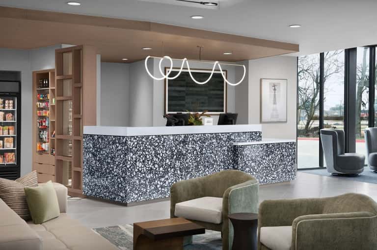 Modern hotel lobby with curved white neon sign, patterned reception desk, and contemporary furniture