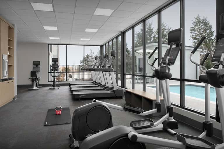 Modern fitness center with cardio equipment, treadmills, and large windows overlooking pool area