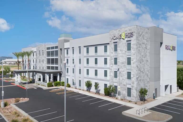 Modern multi-story hotel building with white exterior, palm trees, and parking lot
