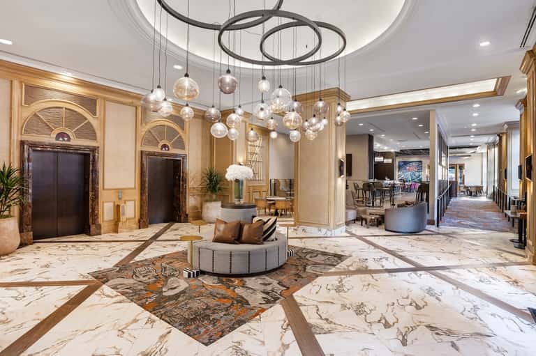Elegant hotel lobby with marble floors, glass chandelier, dark wood doors, and seating