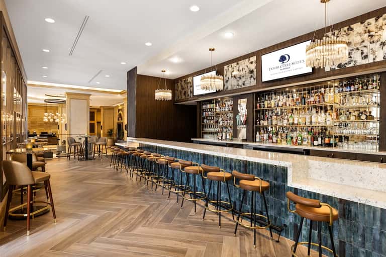 Upscale hotel bar with marble countertop, extensive liquor selection, and elegant chandeliers