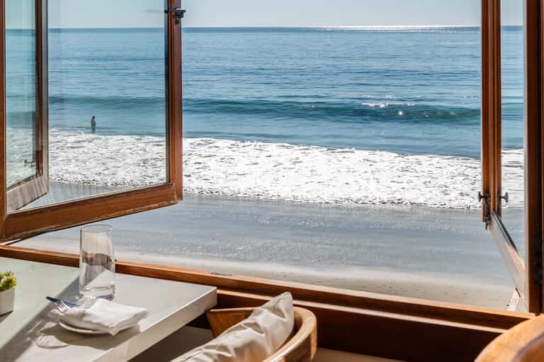 Beachfront dining room with ocean and sandy beach view through open doors