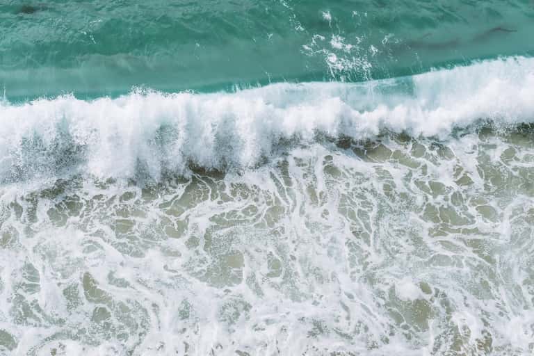Aerial view of turquoise ocean waves with white foam breaking on sandy beach