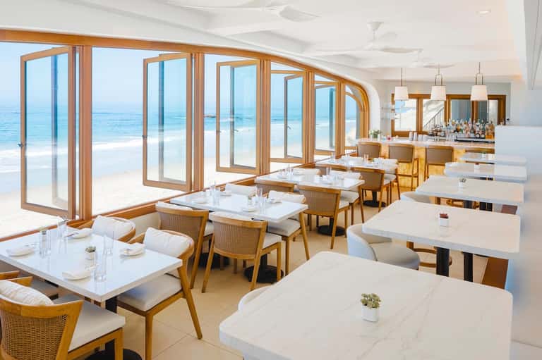 Elegant beachfront restaurant with wooden doors, white tables, and ocean views