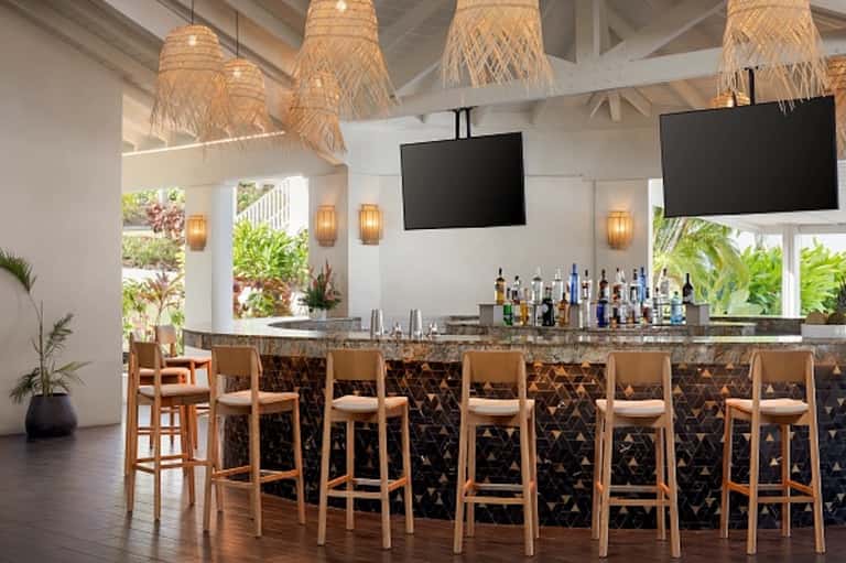Beachfront bar with wooden stools, woven pendant lights, and ocean-view windows