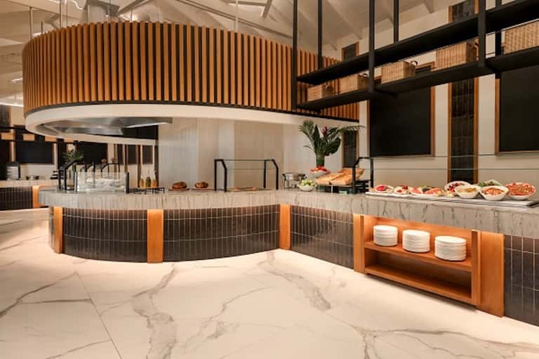 Modern hotel restaurant with curved wooden ceiling, bar seating, and food display