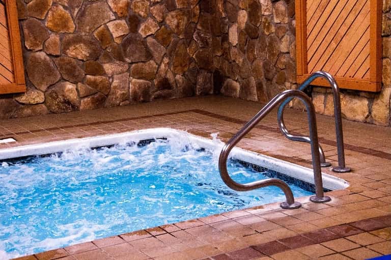 Indoor hot tub with metal handrails surrounded by stone walls and wooden doors